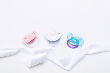 Baby shower with three colorful baby silicone pacifier with holder with ribbon on white background. Mock up. Flat lay. Top view