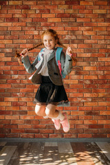 Cute schoolgirl with schoolbag jumps at brick wall
