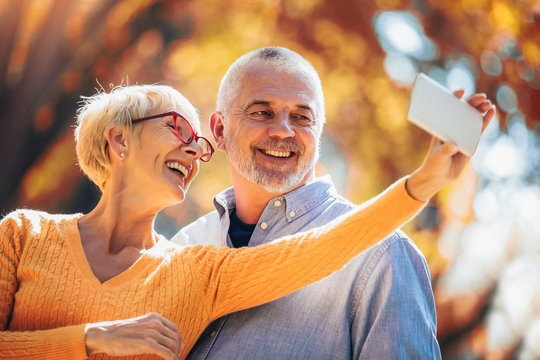 Active Seniors Taking Selfies Of Them Having Fun Outside In The Autumn Forest