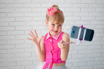 The beautiful girl in pink clothes and a crown takes a selfie on phone. The child shoots video on the canal, the young blogger.