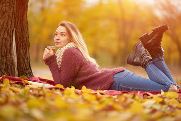 Girl in the autumn park on a warm blanket and with hot tea. Concept of autumn warmth, atmosphere and comfort