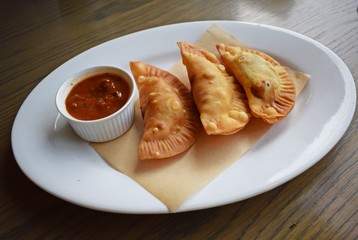 Delicious fried chebureks with sauce on a white plate.