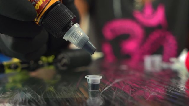 Black ink drops down in slow motion in hands  of Tattoo artist with black gloves