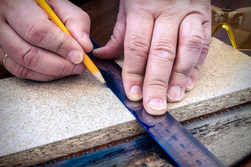 A person marks a wooden board with a pencil and ruler