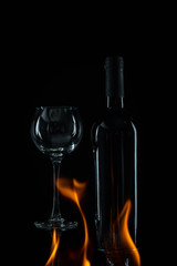 transparent wineglass with bottle and spurts of flame on black background 