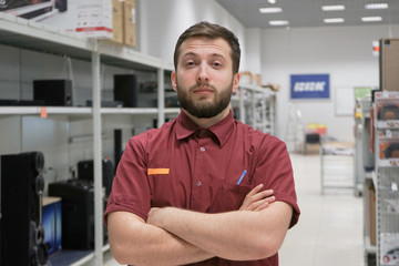 Fototapeta premium Portrait of a Professional Expert Consultant Smiles and Looks into Camera as Stands in the Bright, Modern Electronics Store Full of Latest Models of TV Sets, Cameras, Tablets and other Devices. 