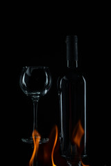 transparent wineglass with bottle and spurts of flame on black background 