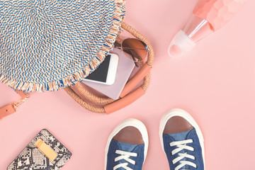 Summer trendy woven straw bag animal print purse with sunglasses, passport sneakers and cell mobile phone on pink background. Summer exotic travel concept. Flat lay with copy space