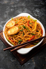 Egg Schezwan/hakka noodles, popular indochinese food served in a bowl with chopsticks. selective focus