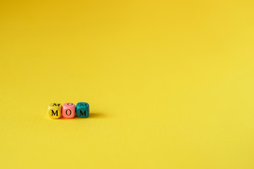Multicolored wooden cubes with the inscription Mom on a yellow background to Mother's Day for greeting card / poster / banner