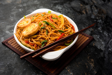 Egg Schezwan/hakka noodles, popular indochinese food served in a bowl with chopsticks. selective focus