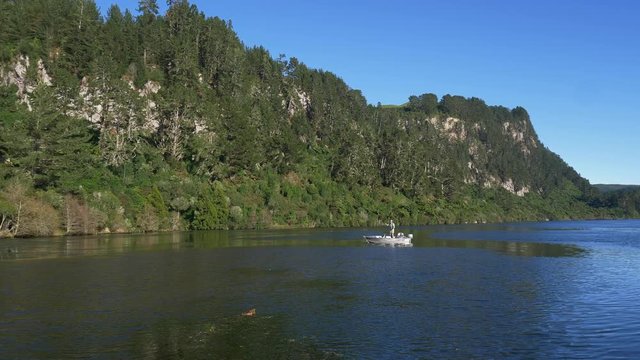 Fly fisherman fishing from drifting boat in pristine lake in New Zealand