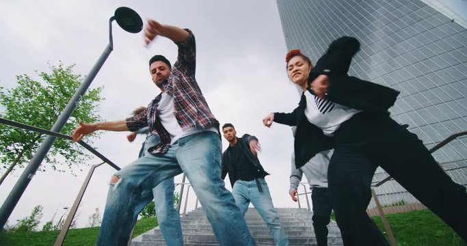 Slow motion of group of young urban dancers of different ethnicities are having fun to training in a city center with skyscrapers.