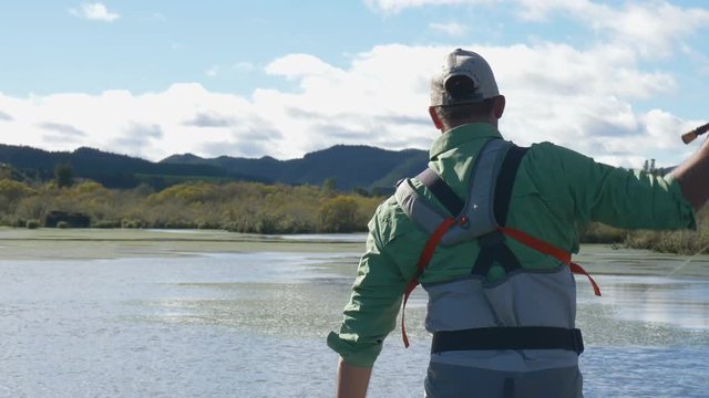 fly fisherman hooks trout while standing on boat