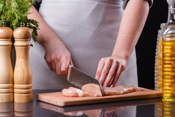 young woman in a gray apron cuts chicken breast
