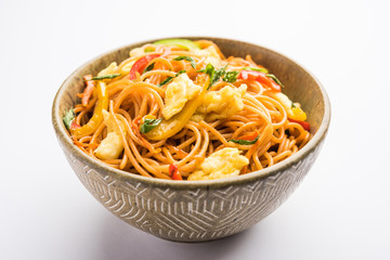 Egg Schezwan/hakka noodles, popular indochinese food served in a bowl with chopsticks. selective focus