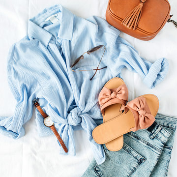 Feminine summer fashion composition with blouse, slippers, purse, sunglasses, watch, jean shorts on white background. Flat lay, top view minimalist clothes collage. Female fashion blog.