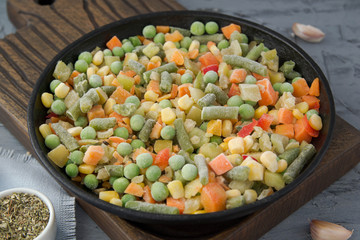 Frozen chopped vegetables in a boiling pan with spices. Vegan food.
