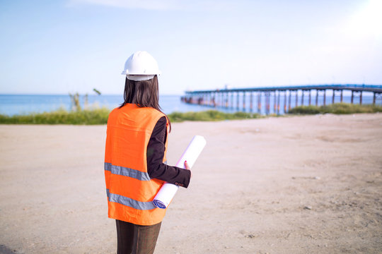Ingegnere donna giovanissima di spalle su un pontile industriale sull'Oceano.