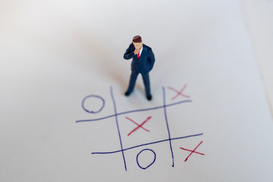 Business direction and planning concept. Businessman miniature figure standing and thinking on paper with OX (tic tac toe) board game.