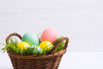 Easter wicker basket with colored pastel eggs decoration. Copy space. White wooden background. Selective focus