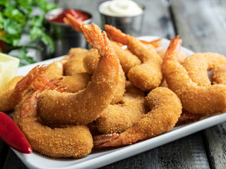 fried breaded shrimps served with lime and coriander leaves on white plate on wooden table, delicious deep, red, white sauce
