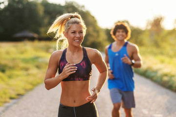 Cute sporty couple running in nature on the sunny summer day. Selective focus on blonde woman with...