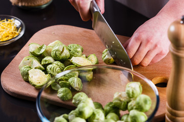 young woman cuts Brussels sprouts on a wooden cutting board