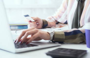 Female office worker hands holding credit card, typing on the keyboard of laptop, online shopping detail close up.