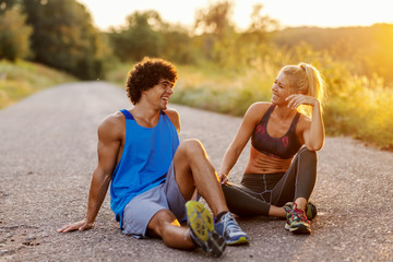 Smiling beautiful sporty couple in love sitting on the country road and resting on sunny summer day.