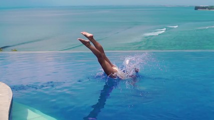 An active young woman in a swimsuit dives into the pool and splashes glassy water. Girl jumping into the pool while relaxing in a tropical resort on the background of green palm trees and the ocean - Powered by Adobe