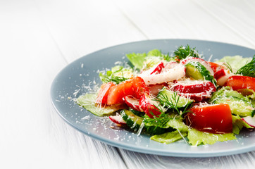 Fresh spring vegetable salad with radish and parmesan. Plate with salad on a white wooden table.