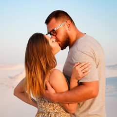 lovely attractive couple kissing on the white sand beach or in the desert or in the sand dunes, happy couple embracing at the beach on a sunny day, couple in love