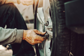 Close up of auto mechanic changing tire while crouching at workshop.