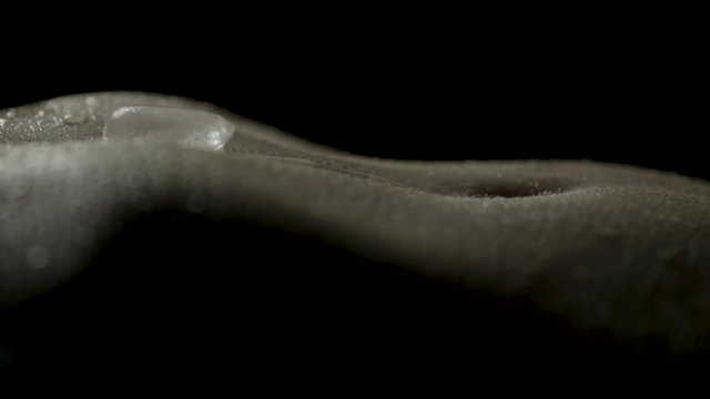 Extreme close-up of woman's sweat covered stomach as an ice cube melts and slides into her navel