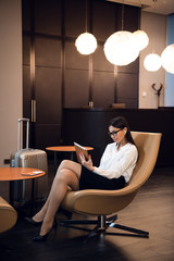 Confident businesswoman listening music on her tablet computer while sitting in chair in airport business lounge - 263755516