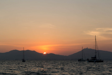 Sunset and dawn at sea against a backdrop of mountains and boats