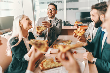 Small group of happy colleagues in formal wear chatting and eating pizza together for lunch. Talent...
