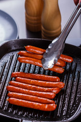 young woman in a gray apron fries sausages