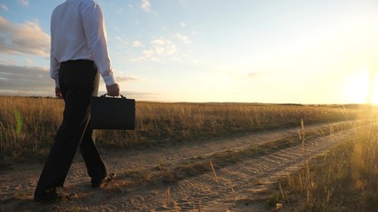 businessman in sunglasses goes down the country road with a briefcase in his hand. The entrepreneur...