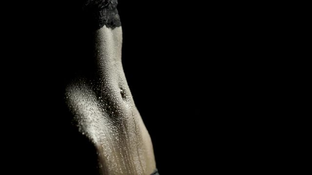 Close-up of a woman's toned abs as sweat drips down with dramatic lighting and black background