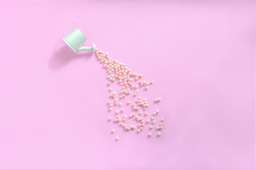 Sprayed watering can with of candy on pink background. Round sweet peas sprinkle. Creative sweet concept. Flat lay, top view, copy space
