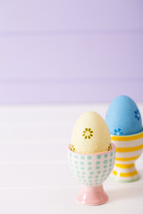 Two colorful painted Easter eggs in vibrant modern egg stands on pastel lilac background.
