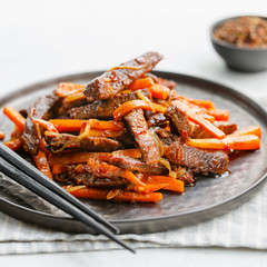 Close-up of Chinese spicy Szechuan beef meal on a black plate with wooden sticks over white table. Asian food recipe, portion for one person.