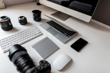 White desktop of a designer with a laptop with a mouse with a modern professional camera with a keyboard with a laptop with a graphic tablet with a computer. Stylish workplace.
