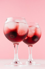 Elegant summer fresh red bright drinks with ice cubes, blueberry on fashion pastel pink color background and white wood table, vertical.