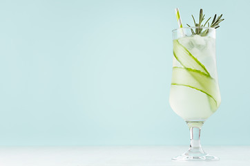 Summer fresh detox cucumber cocktail in wineglass with ice cubes, rosemary, straw on pastel mint...