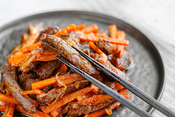 Close-up of Chinese spicy Szechuan beef meal on a black plate with wooden sticks over white table. Asian food recipe, portion for one person.