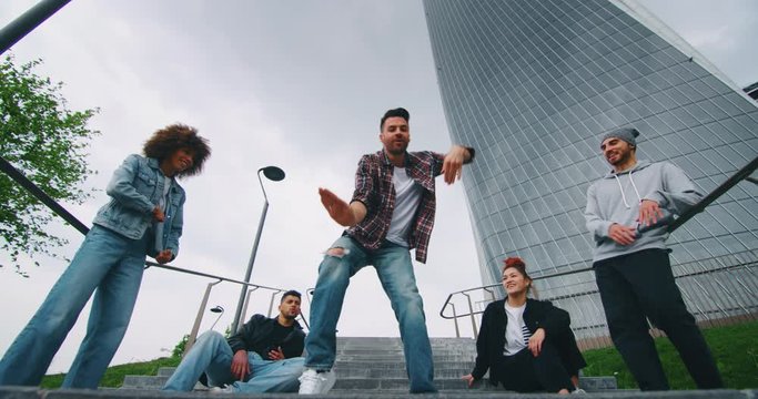 Slow motion of group of young urban dancers of different ethnicities are having fun to training in a city center with skyscrapers.