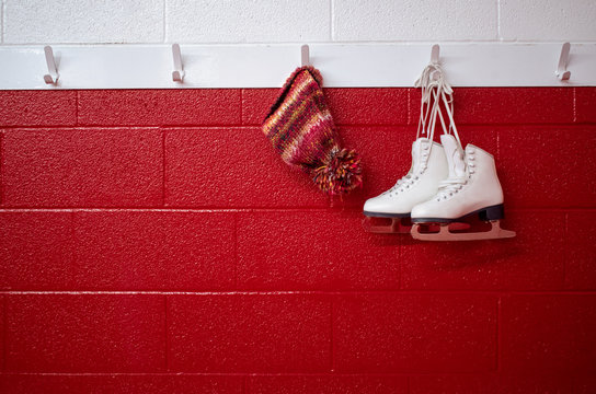Figure skates hanging over red wall in locker room with winter hat and copy space 